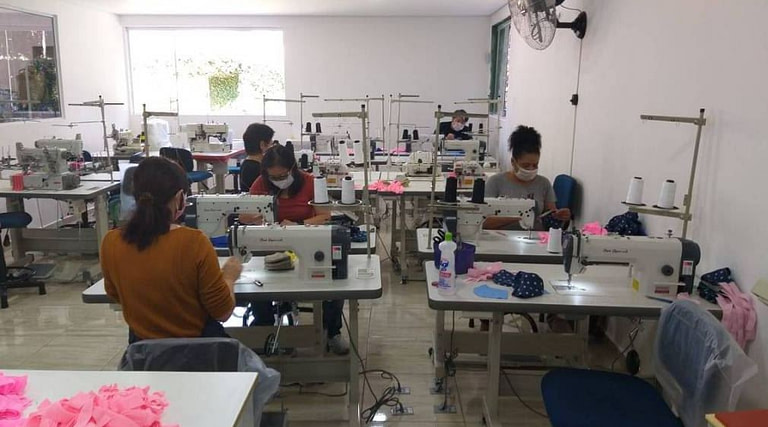 Mulheres costuram em máquinas em sala de costura